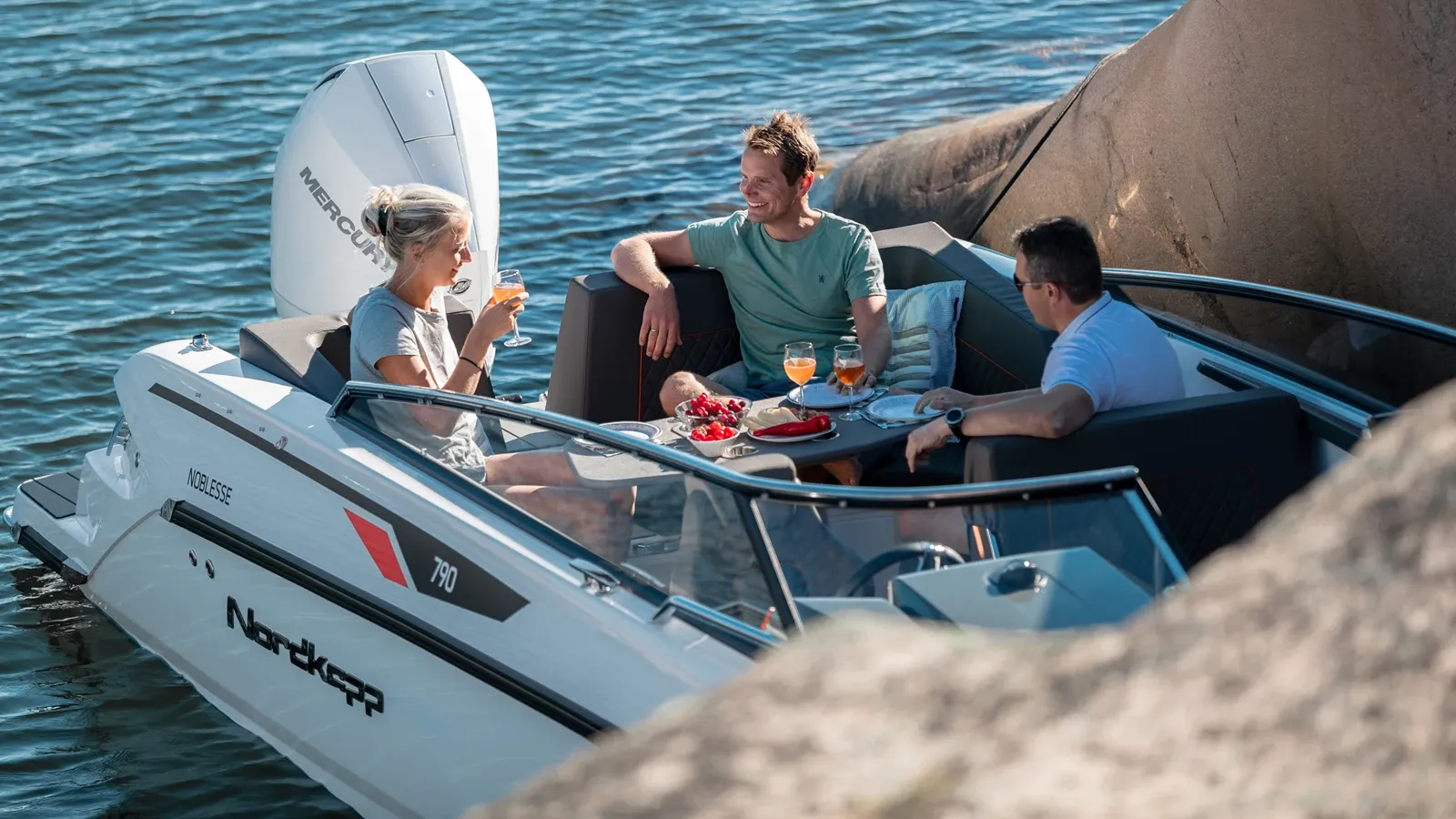 Nordkapp Noblesse 790 moored next to rocks with people using the back seats and table
